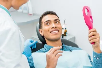 man holding up a mirror looking at his freshly cleaned smile thanks to Little Mountain Dental