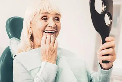 woman looking in the mirror at her new smile thanks to dentures from Little Mountain Dental